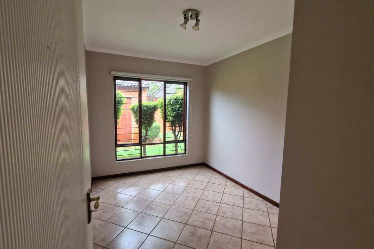 An empty bedroom featuring neutral wall paint, tiled flooring, and a window fitted with security bars, offering a clean and versatile living space.