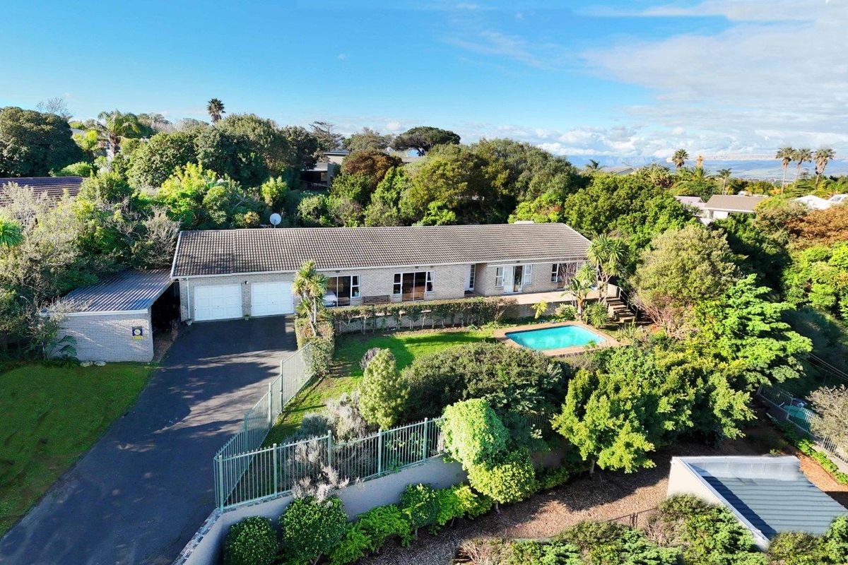 Aerial view of a single-story brick residence featuring a swimming pool, established garden, and a double garage with a paved driveway.