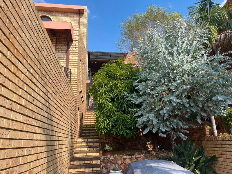 A rear exterior view featuring a brick staircase leading up alongside a brick retaining wall and established garden landscaping.