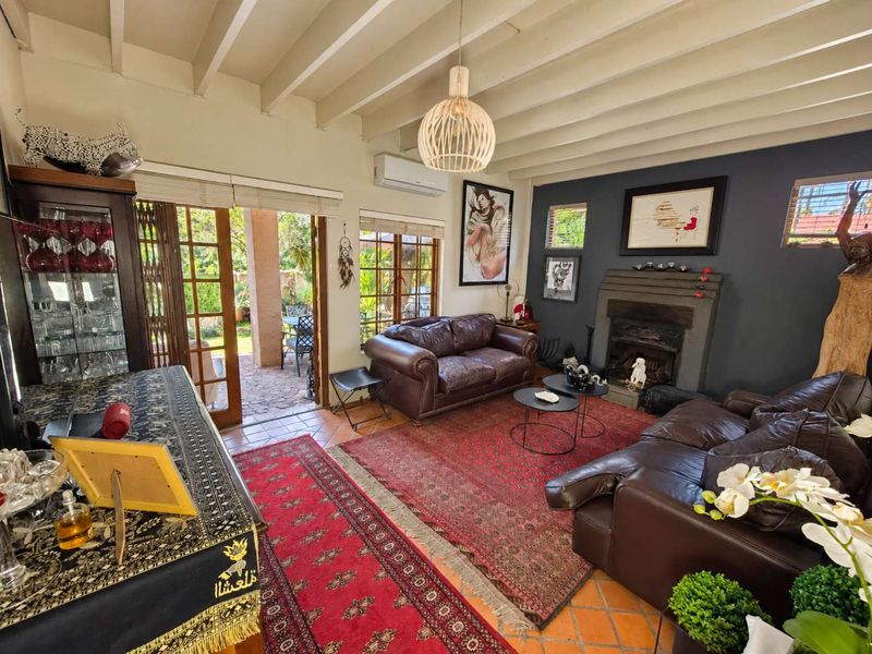 A cozy living room featuring exposed beam ceilings, terracotta flooring, a traditional fireplace, and direct access to an outdoor patio through french doors.
