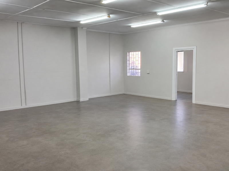 A spacious, clean, and empty industrial utility space featuring smooth concrete flooring, bright fluorescent lighting, and secure window bars.
