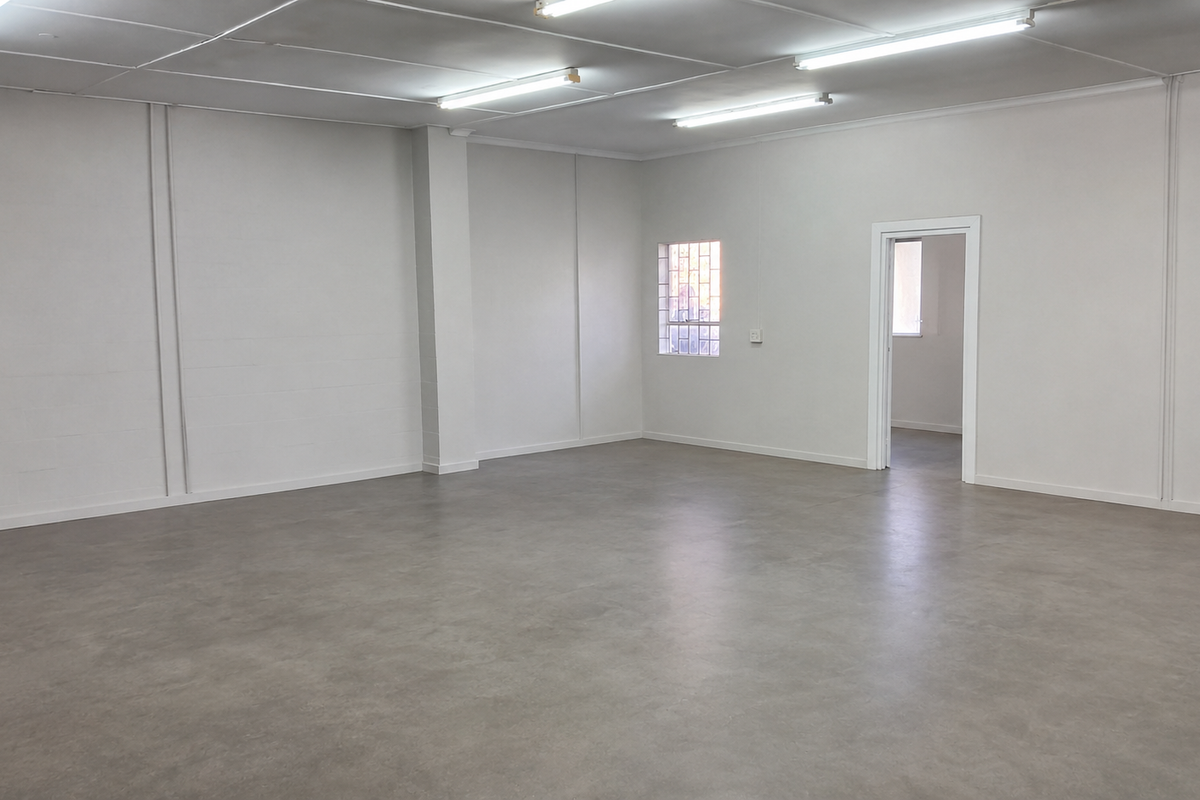 A spacious, clean, and empty industrial utility space featuring smooth concrete flooring, bright fluorescent lighting, and secure window bars.