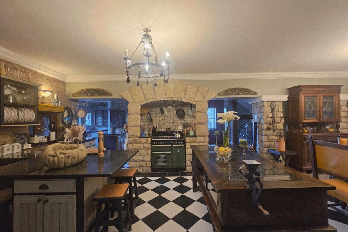 A rustic-style kitchen featuring a stone-encased range cooker, checkerboard flooring, granite countertops, and a central island with integrated cabinetry.