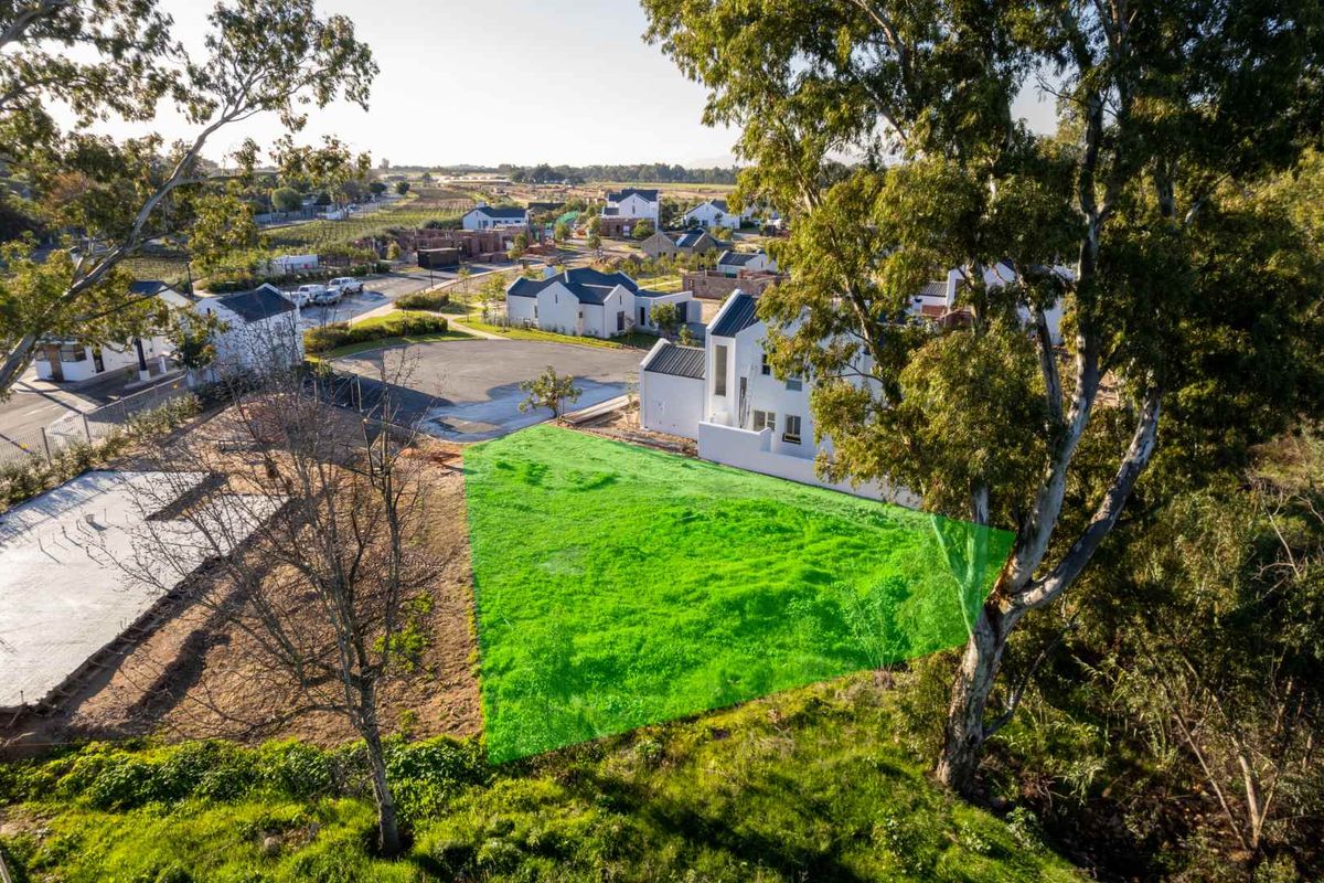 Aerial view of a vacant residential plot highlighted in green, situated within a developed estate with surrounding infrastructure and mature trees.