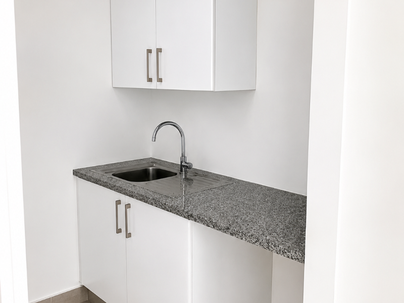 A clean, modern kitchenette featuring white built-in cabinetry, a granite countertop, and a stainless steel sink, suitable for office use.