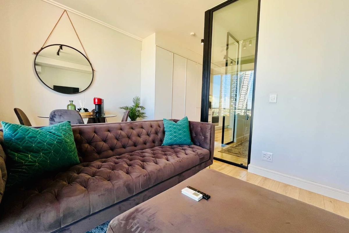 A modern living area featuring light wood-look flooring, built-in cabinetry, and a sleek black-framed glass partition leading to an adjacent space.