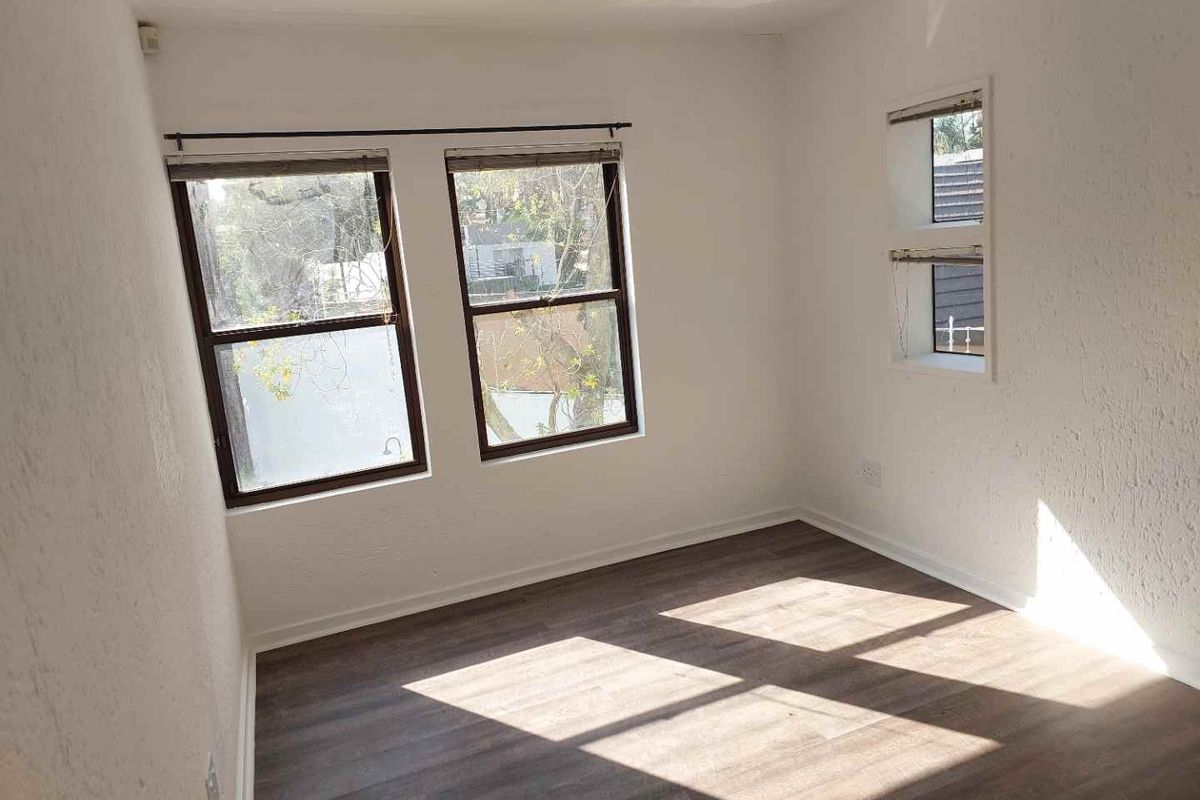 A bright, empty bedroom featuring modern laminate flooring and multiple windows providing natural light.