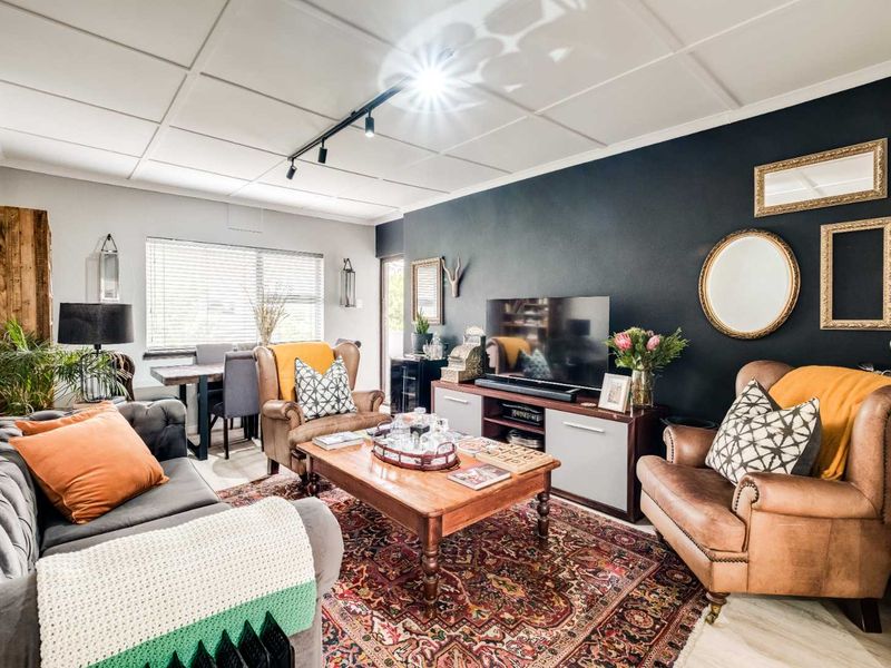 An open-plan living and dining area featuring a dark accent wall, track lighting, and a tiled ceiling, creating a cozy and well-defined living space.