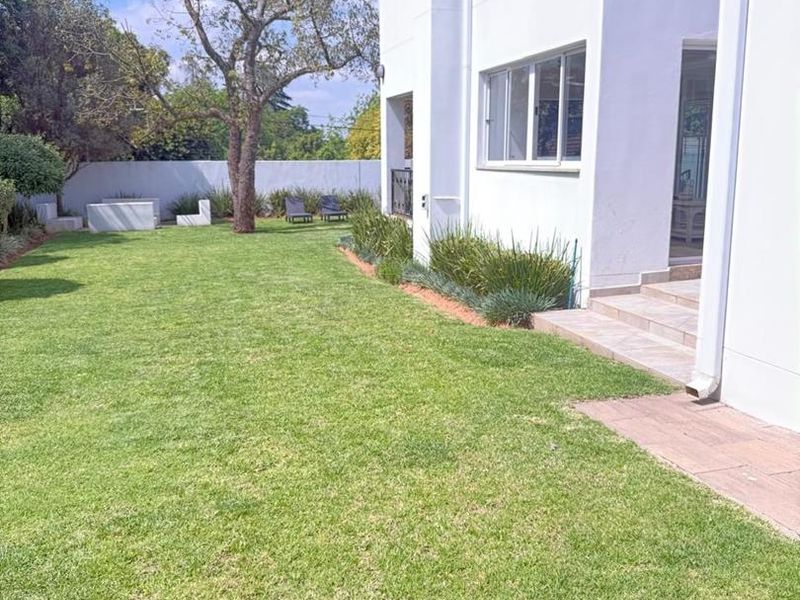 A well-maintained rear garden featuring a manicured lawn, boundary wall, and a paved patio area adjacent to the house exterior.
