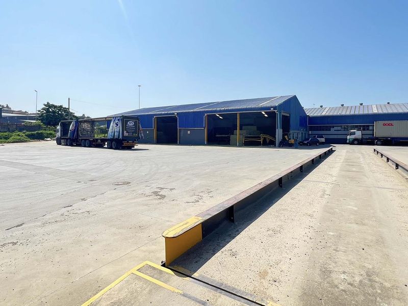 Expansive industrial yard featuring a large concrete loading area, steel guide rails, and multiple warehouse bays with high-clearance access.