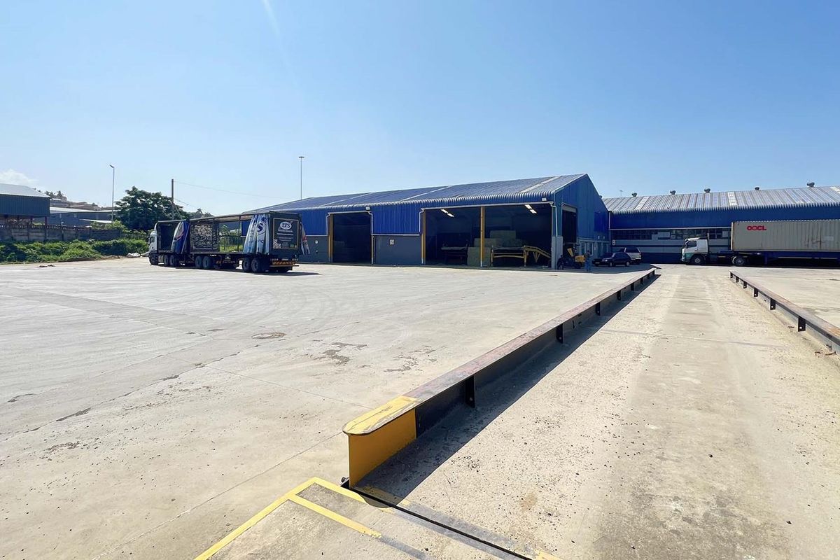 Expansive industrial yard featuring a large concrete loading area, steel guide rails, and multiple warehouse bays with high-clearance access.