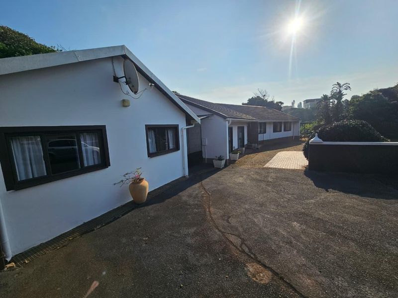 Front exterior view of the house featuring an asphalt driveway, paved walkway, and boundary wall under a clear sky.