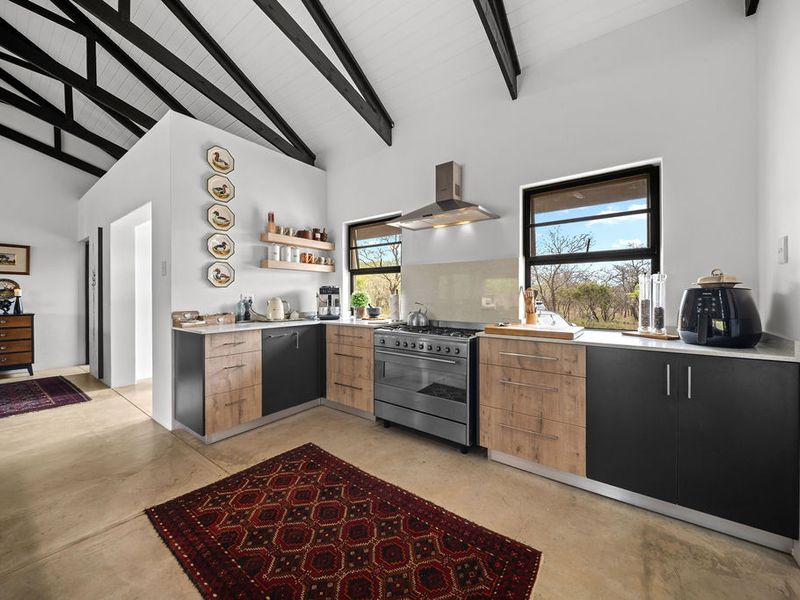 Modern kitchen featuring two-tone cabinetry, stone countertops, a gas stove with extractor fan, and striking exposed timber beams under a vaulted ceiling.