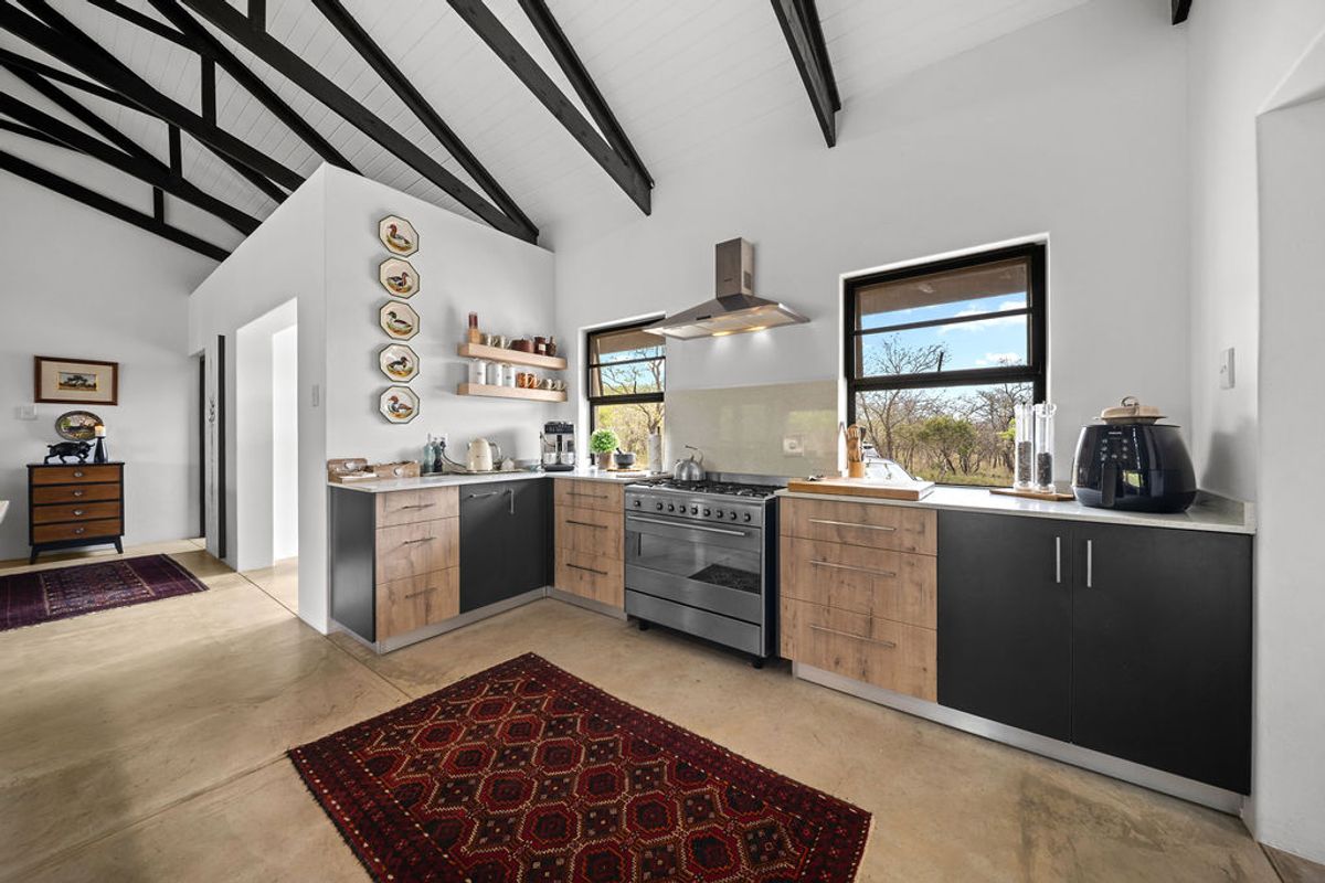 Modern kitchen featuring two-tone cabinetry, stone countertops, a gas stove with extractor fan, and striking exposed timber beams under a vaulted ceiling.