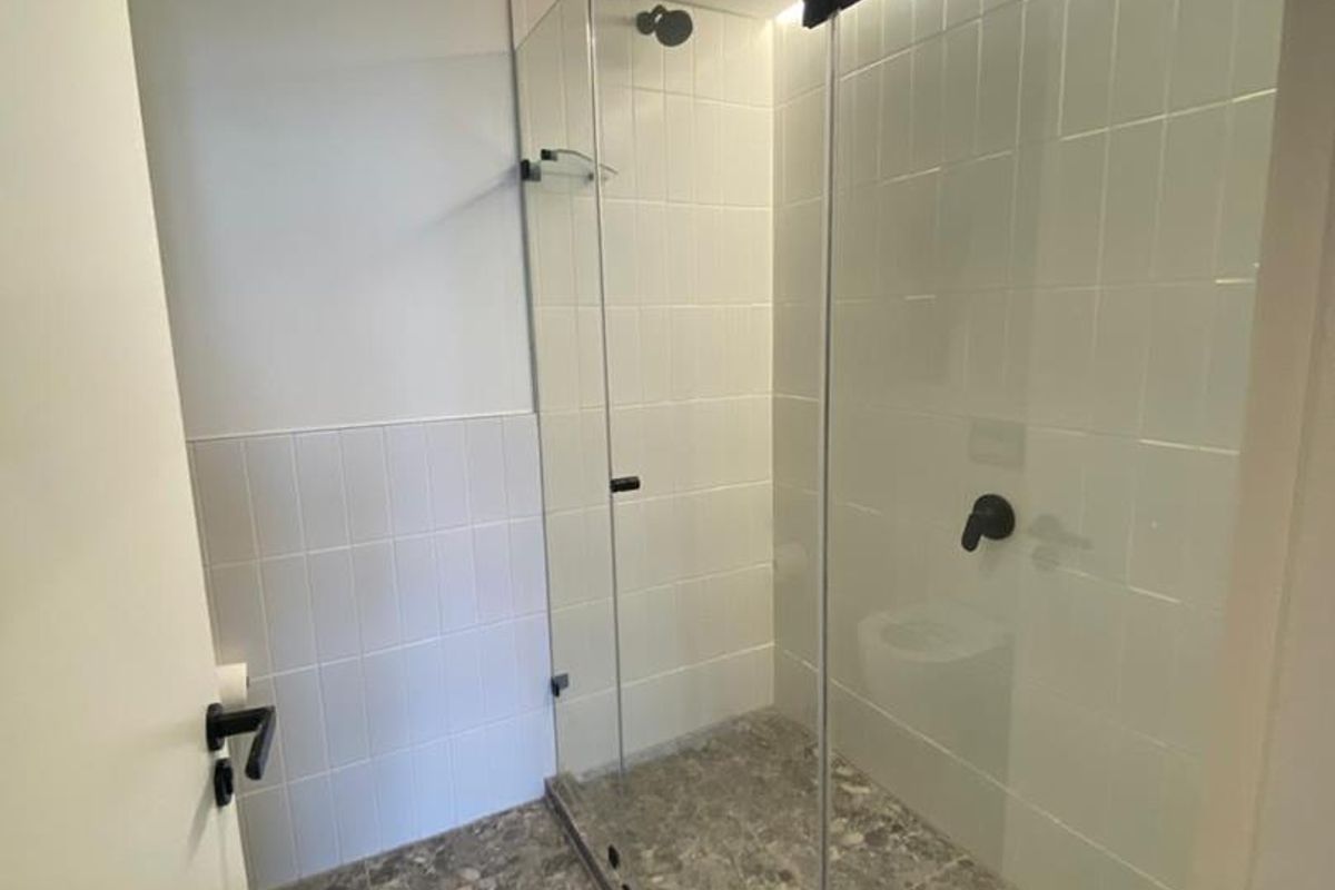 Modern bathroom featuring a walk-in shower with glass enclosure, matte black fixtures, and contemporary grey stone-look floor tiling.