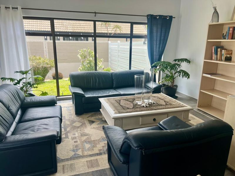A bright living room featuring large floor-to-ceiling windows that provide natural light and a view of the private garden area.