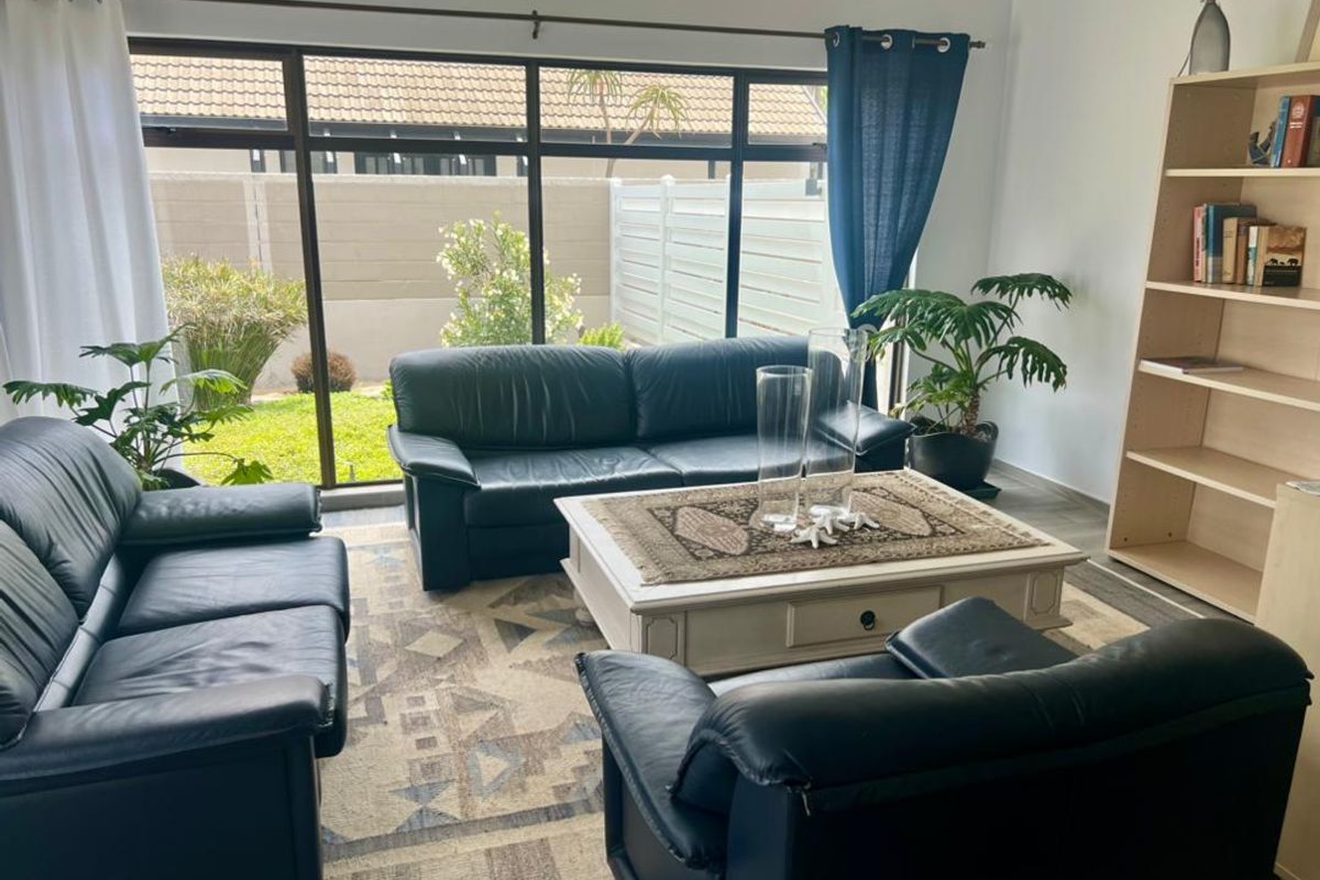 A bright living room featuring large floor-to-ceiling windows that provide natural light and a view of the private garden area.