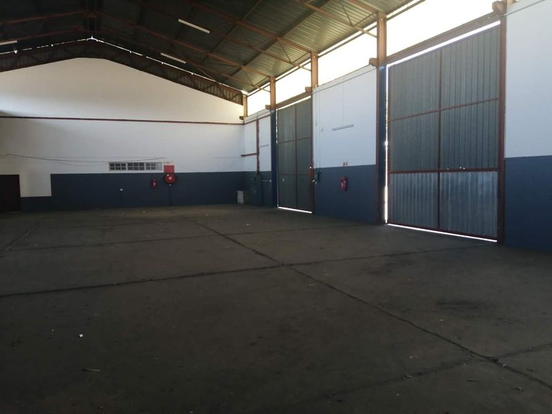 Spacious industrial warehouse unit featuring high ceilings with exposed steel trusses, concrete flooring, and large sliding access doors.