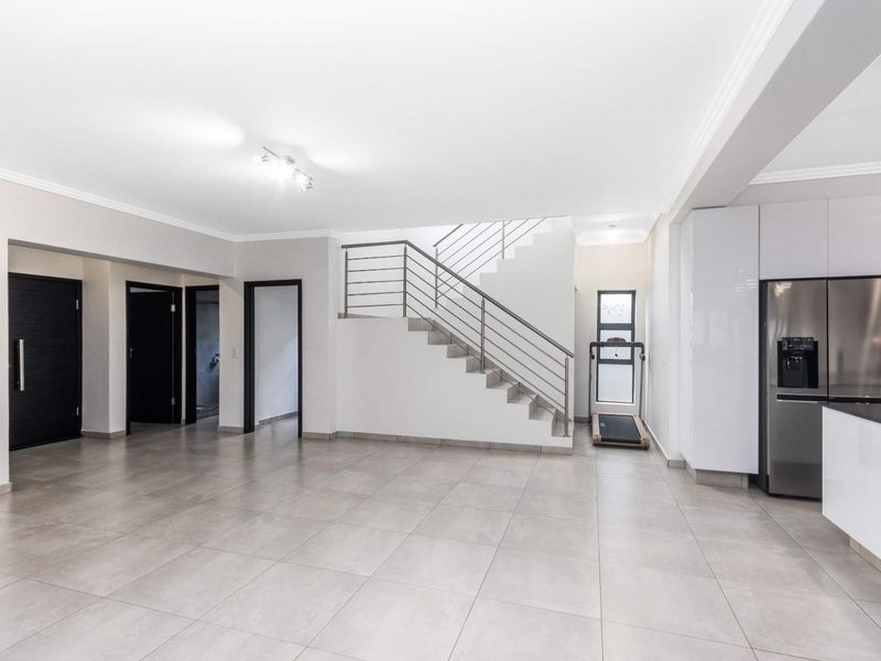 Spacious open-plan living area featuring modern tiled flooring, a central staircase with stainless steel balustrades, and sleek built-in cabinetry.