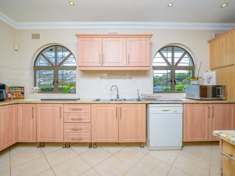 A functional kitchen featuring light wood-tone cabinetry, granite countertops, double sink, and distinctive arched windows providing natural light.