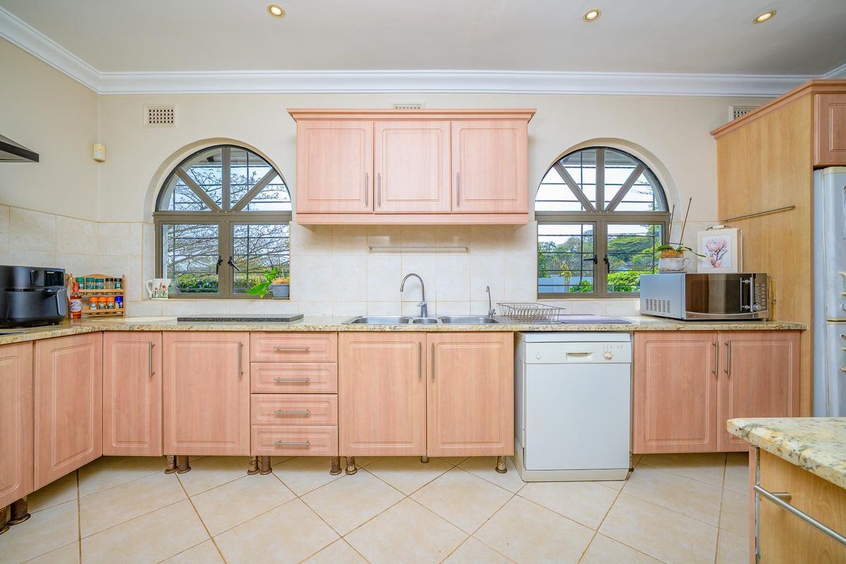 A functional kitchen featuring light wood-tone cabinetry, granite countertops, double sink, and distinctive arched windows providing natural light.