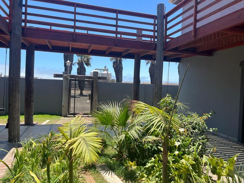 A rear courtyard area featuring a raised timber deck, support posts, and a landscaped garden with a secure metal gate.