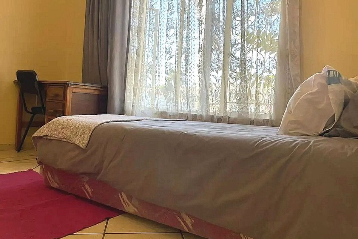 A bedroom featuring tiled flooring and a large window allowing natural light, providing a functional space for rest.