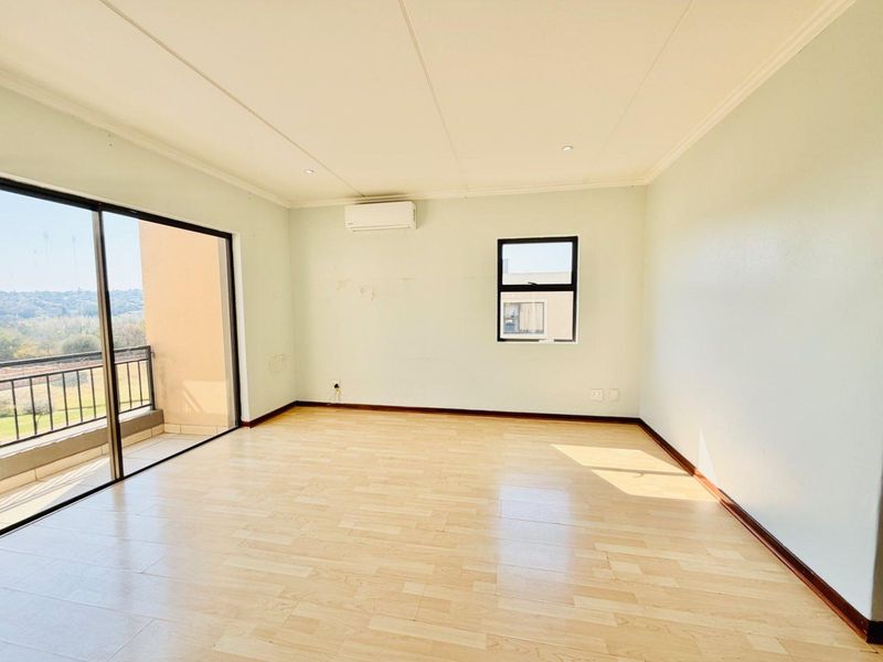 An empty, light-filled living room featuring laminate flooring, an air conditioning unit, and large sliding glass doors leading to a private balcony.