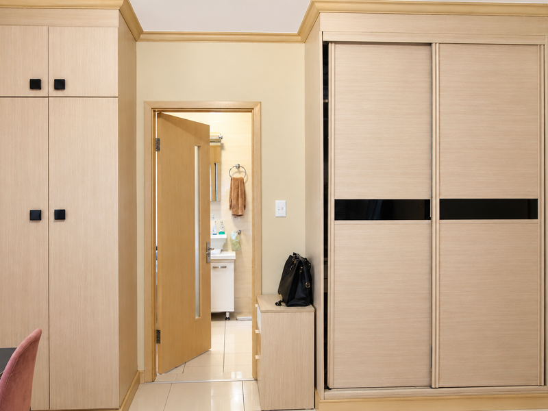 A well-maintained hallway featuring extensive built-in light wood cabinetry and wardrobes, with tiled flooring and access to an adjacent bathroom.