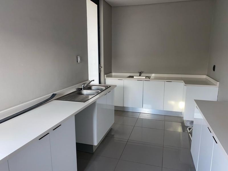 A clean, modern scullery featuring white cabinetry, stone countertops, and dual sink areas with tiled flooring.