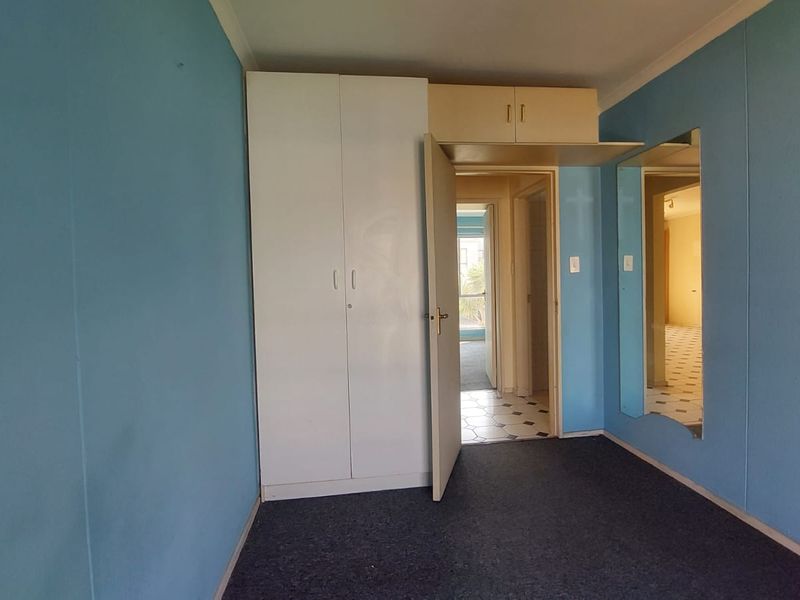 An empty bedroom featuring built-in wardrobes with overhead storage, blue painted walls, and carpet flooring, offering a blank canvas for renovation.