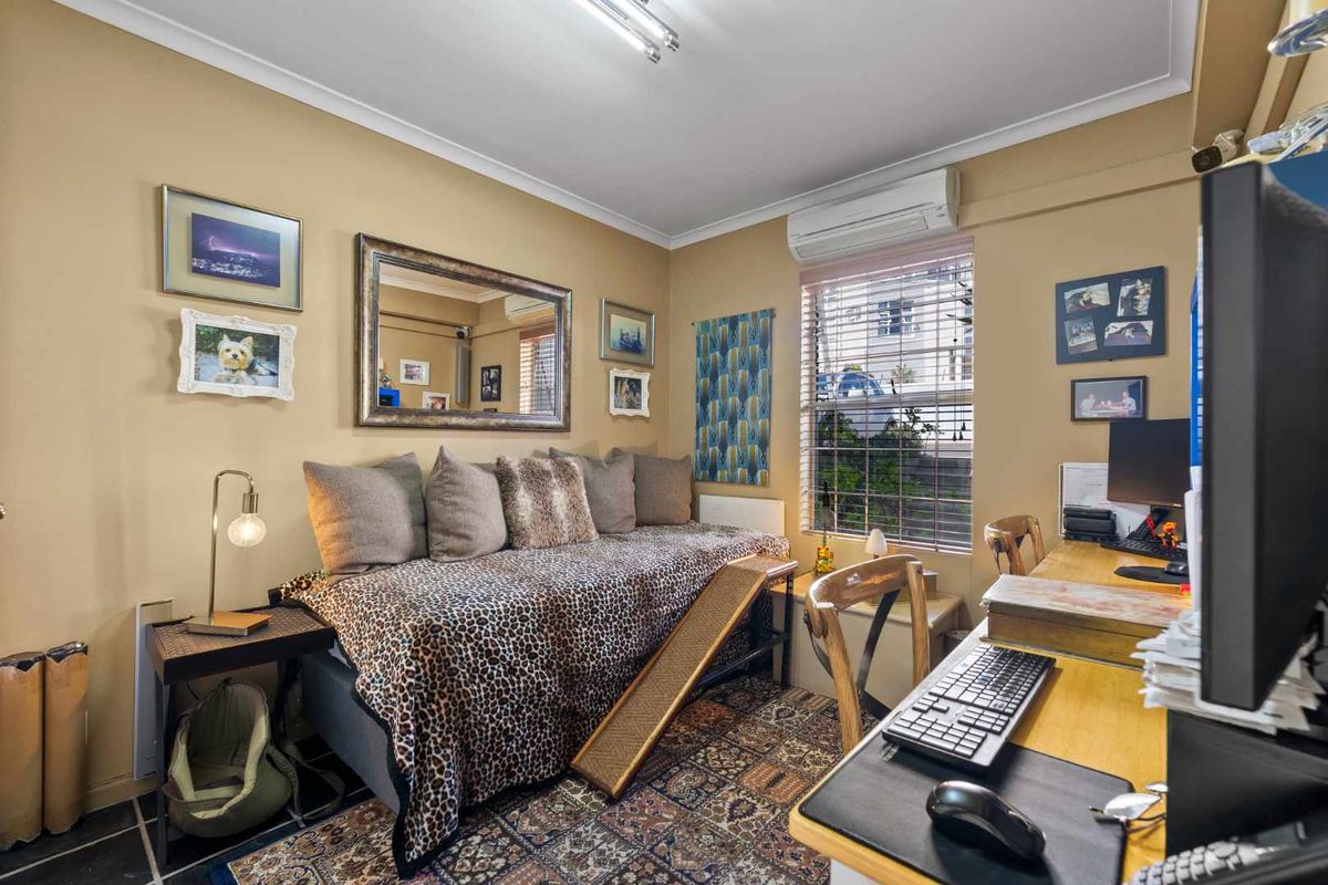 A functional bedroom featuring tiled flooring, a wall-mounted split-system air conditioner, and a window with venetian blinds.