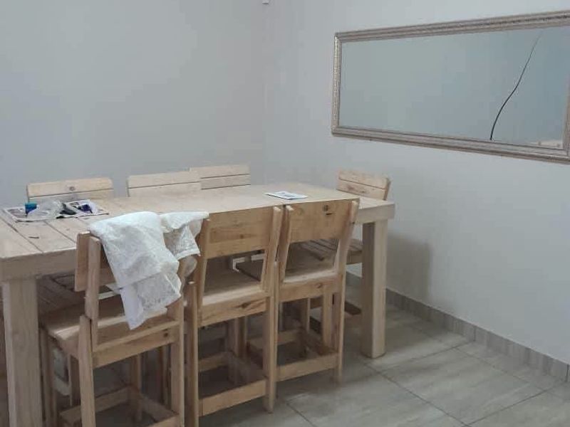 A simple dining area featuring neutral wall paint, tiled flooring, and a coved ceiling, currently furnished with a wooden dining set.