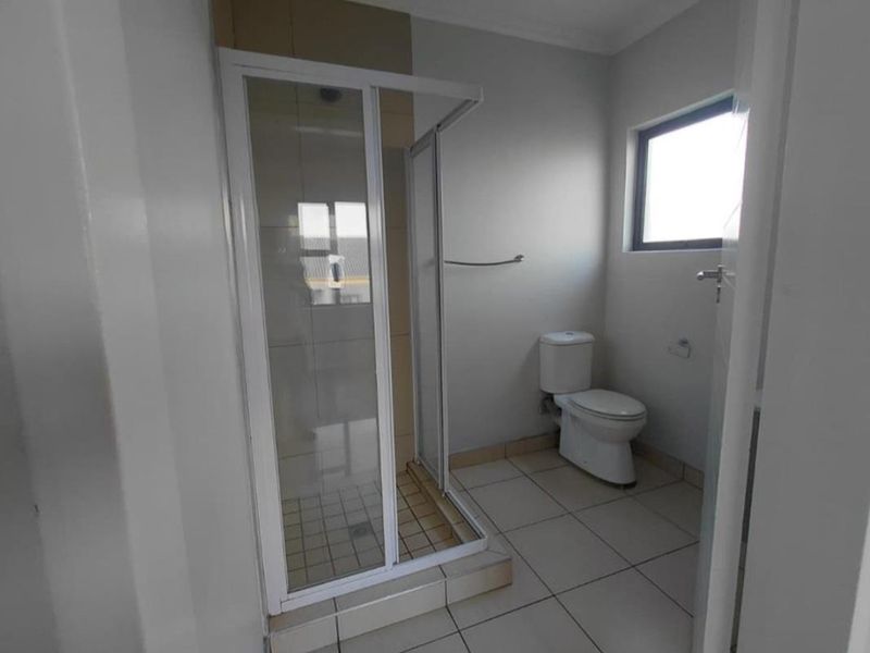 A functional bathroom featuring a glass shower enclosure, a standard toilet, and neutral floor tiling.