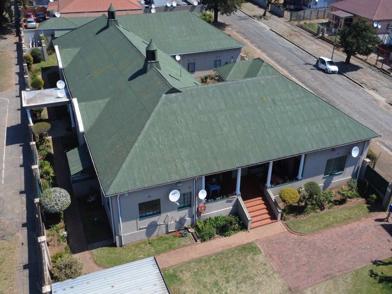 Aerial view of a residential property featuring a large corrugated metal roof, a covered veranda with concrete columns, and a brick paved driveway.