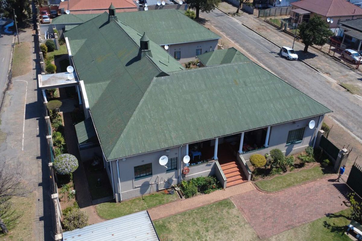 Aerial view of a residential property featuring a large corrugated metal roof, a covered veranda with concrete columns, and a brick paved driveway.