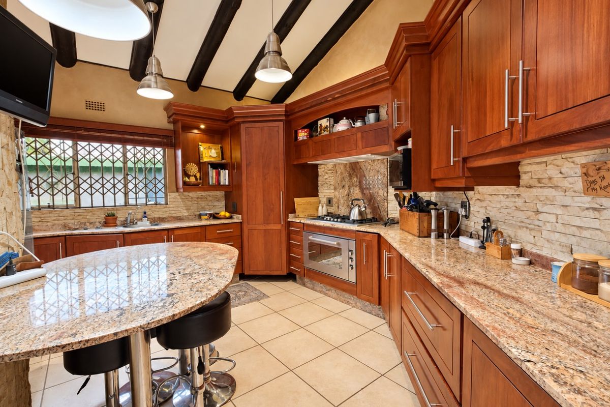 Spacious kitchen featuring warm wooden cabinetry, granite countertops, exposed timber ceiling beams, and a functional layout with a built-in oven and gas hob.