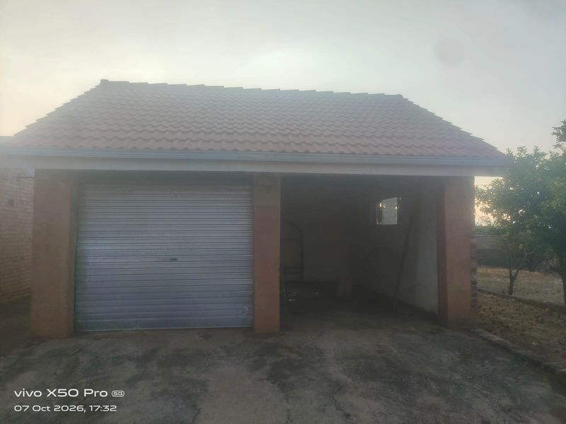 A detached garage featuring a roller shutter door, tiled roof, and concrete driveway, showing signs of wear and weathering.