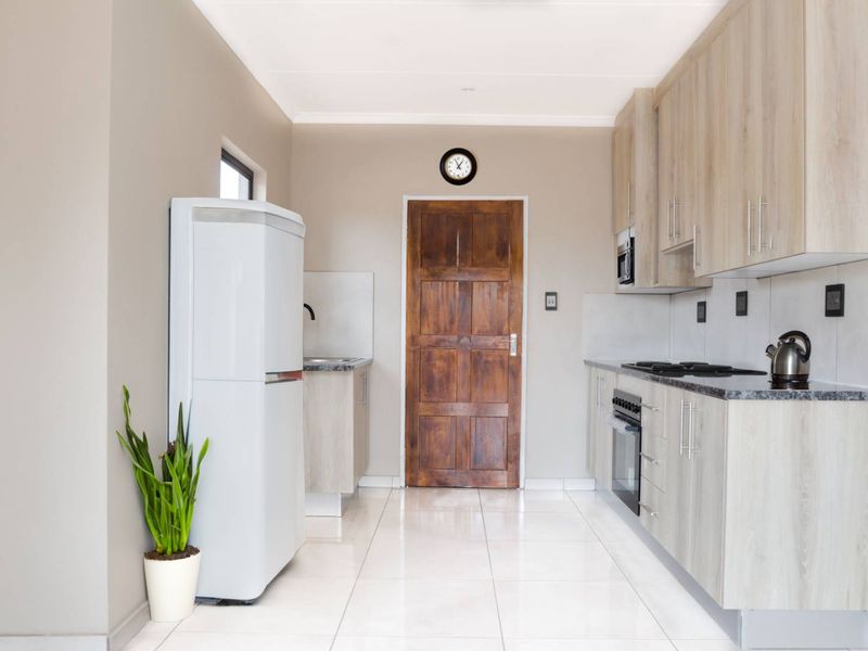 A modern, well-maintained kitchen featuring light wood-finish cabinetry, granite countertops, built-in oven and hob, and clean tiled flooring.