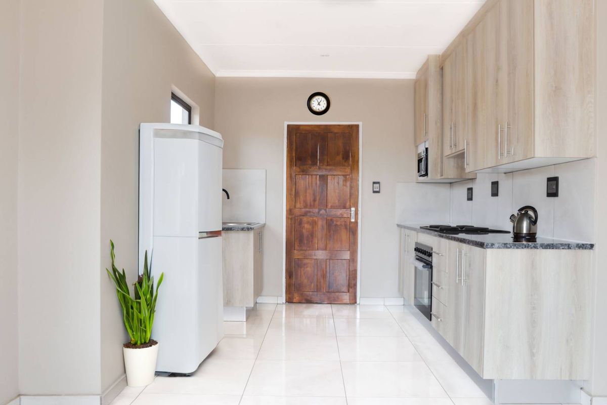 A modern, well-maintained kitchen featuring light wood-finish cabinetry, granite countertops, built-in oven and hob, and clean tiled flooring.
