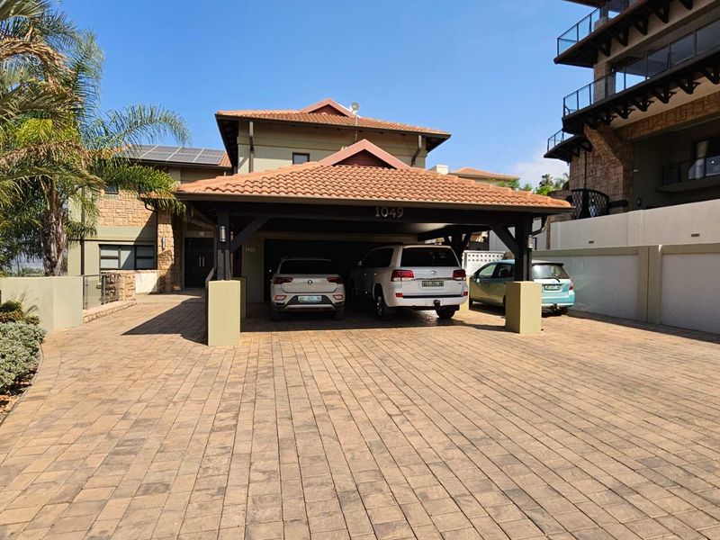 Front exterior view of the property featuring a spacious paved driveway, a covered carport, and stone-clad architectural details.