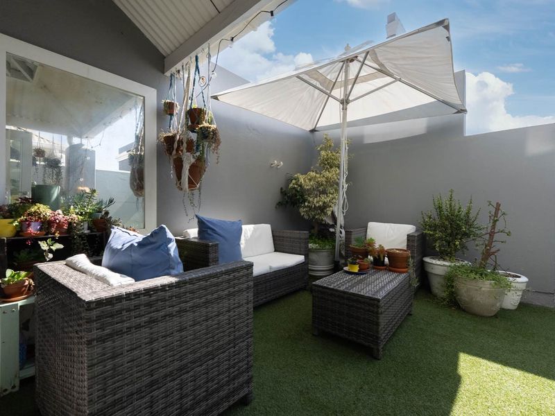 A private covered patio area featuring artificial turf flooring and painted masonry walls, providing a cozy outdoor space for relaxation.
