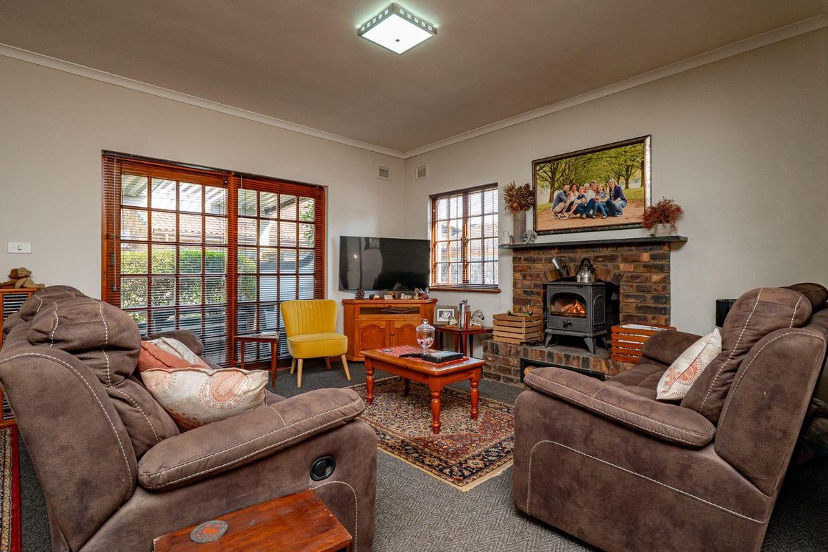 Cozy living room featuring a traditional brick fireplace with a wood-burning stove, timber-framed windows, and sliding glass doors leading to the exterior.