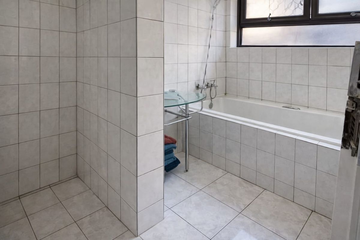 A functional bathroom featuring a built-in bathtub with shower mixer and tiled wall finishes.