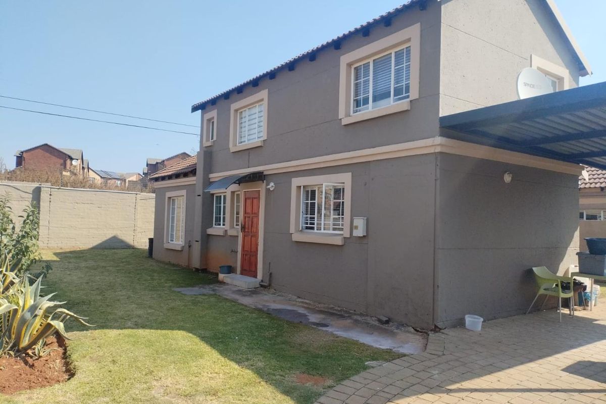 Rear view of a two-story residential property featuring plastered walls, a paved driveway, a carport, and a private garden area with boundary walling.