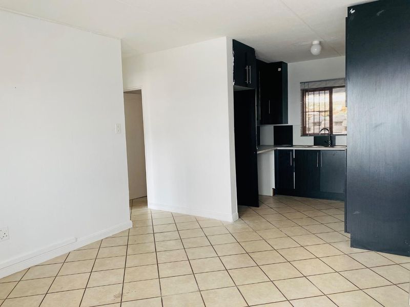 An open-plan living and kitchen area featuring dark cabinetry, tiled flooring, and neutral walls, offering a blank canvas for potential interior design updates.