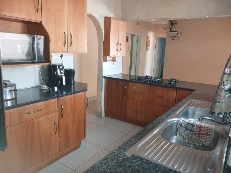 Functional kitchen featuring wooden cabinetry, granite countertops, a gas hob, and a double stainless steel sink, with tiled flooring and an open archway design.