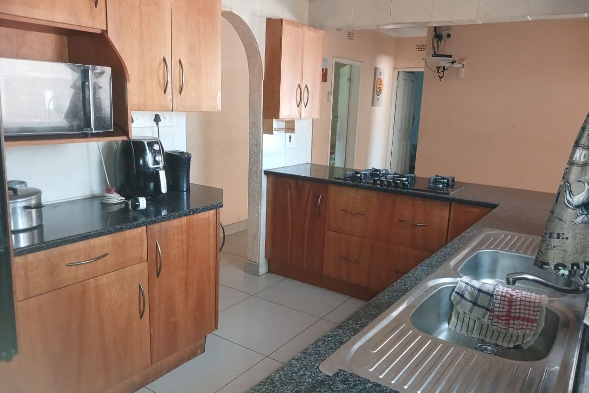Functional kitchen featuring wooden cabinetry, granite countertops, a gas hob, and a double stainless steel sink, with tiled flooring and an open archway design.
