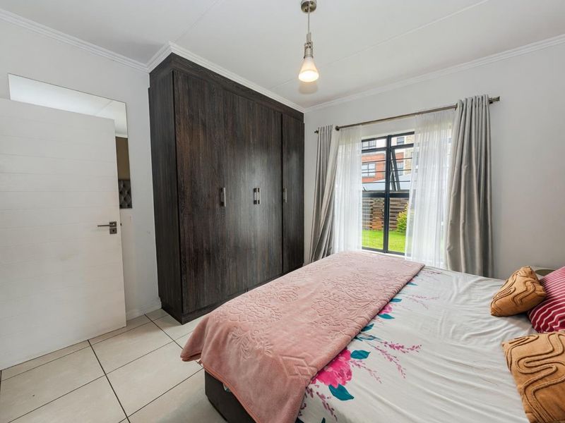 A well-maintained bedroom featuring tiled flooring, a large dark wood built-in wardrobe, and a window providing natural light.
