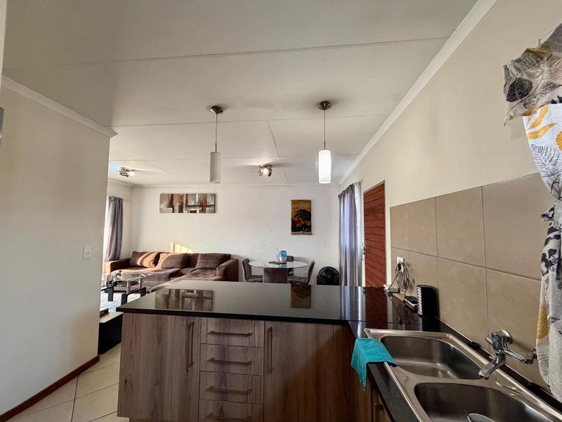 Open-plan living area featuring a modern kitchen with granite countertops, double sink, and tiled backsplash, flowing into a comfortable lounge and dining space.